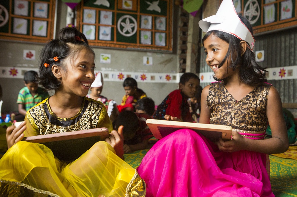 Two girls paint in a classroom in Bangladesh. 