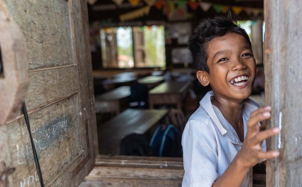 A young boy laughs outside his classroom in Cambodia.