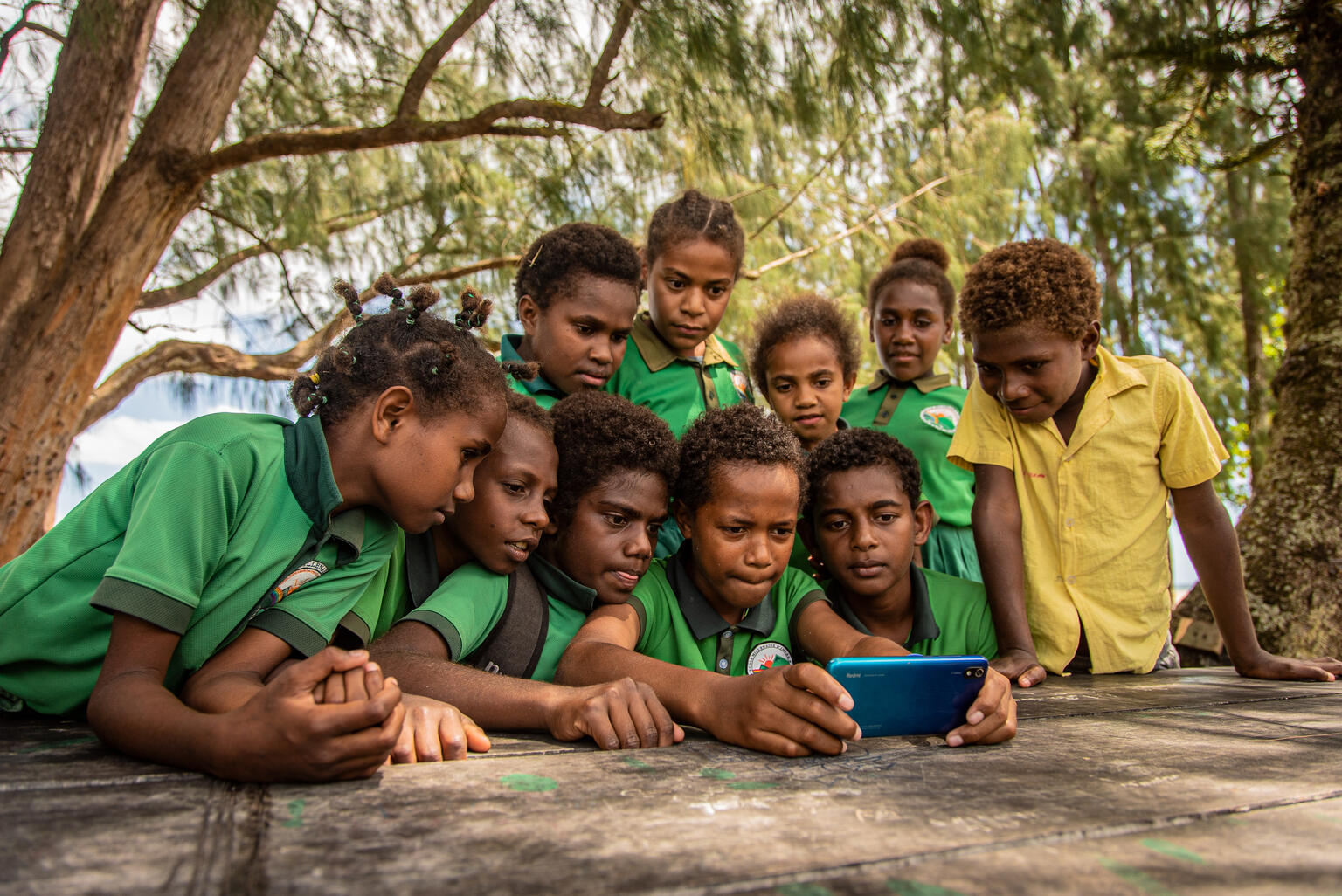 Children in Vanuatu crowd around a cell phone.